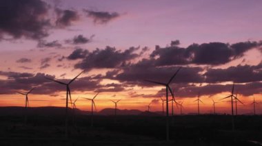 Enerjiyi Kurtarma Enerjisi 'nin hava görüntüsü 4k video formatında. Gün batımında hava görüntüsü. İHA, güneş doğarken rüzgar türbinlerini güzel bulutlarla görüntüler. Küresel ısınma kavramı ve yeşil enerji.