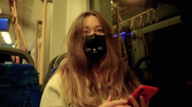 Tıbbi maske takan Çinli bir kız akşam vakti şehir aracına biniyor.