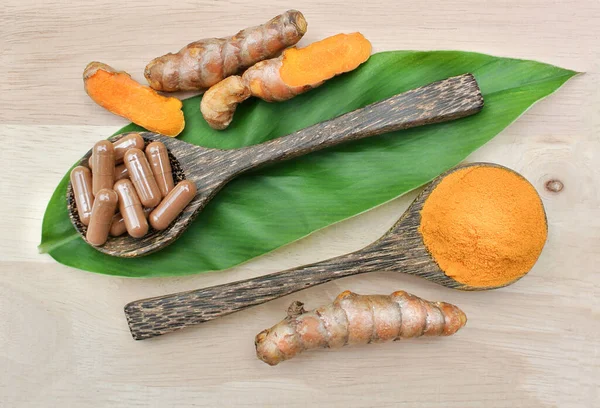 Turmeric powder; Turmeric capsules in a wooden spoon on the leaves and wooden. Turmeric root is herb for good health.Vitamin C for protect virus.