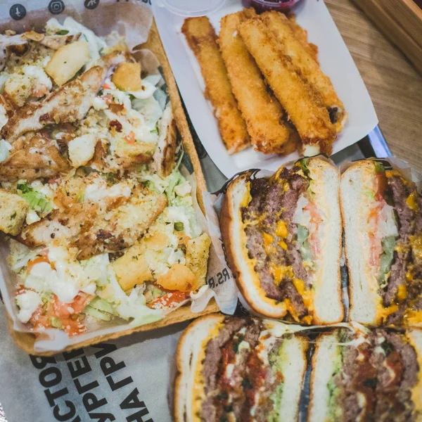 Hamburguesas de carne en rodajas de cerca, ensalada César y palitos de queso mienten — Foto de Stock