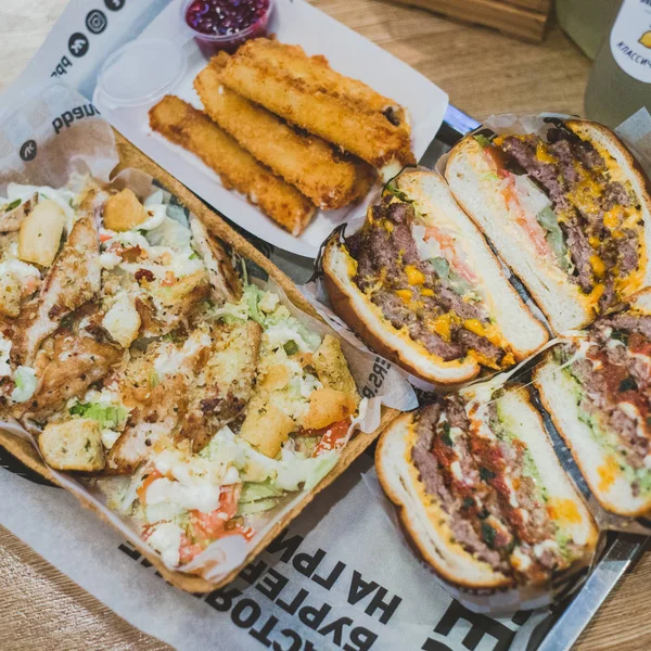 Hamburguesas de carne en rodajas de cerca, ensalada César y palitos de queso mienten — Foto de Stock