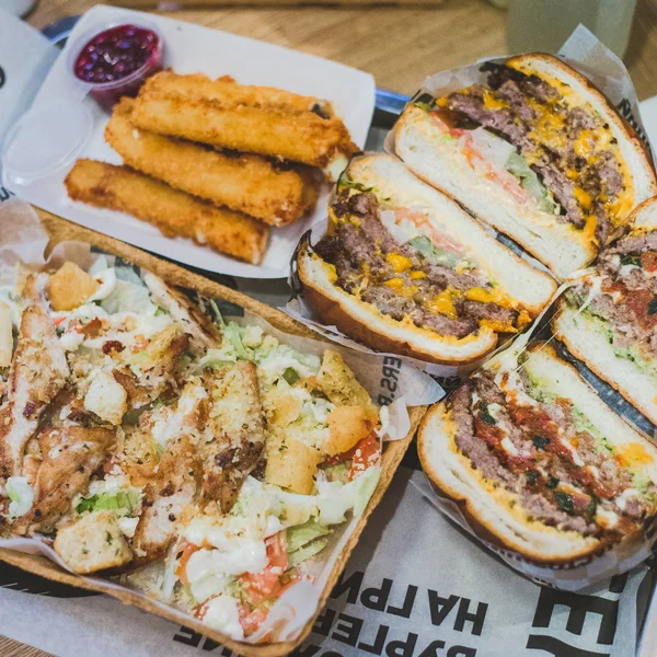 Hamburguesas de carne en rodajas de cerca, ensalada César y palitos de queso mienten — Foto de Stock