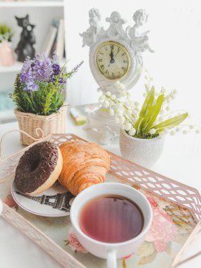 Bir su ısıtıcısı ile bir tepsi, bir fincan çay, bir tabak, kruvasan ve bir do