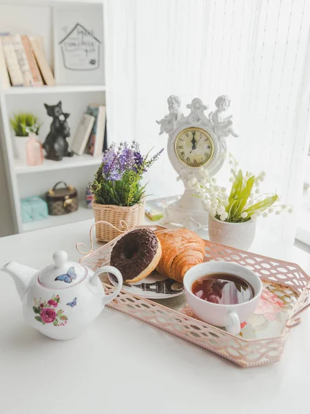 A tálcán egy vízforraló, egy csésze tea, egy csészealj, croissant és egy do — Stock Fotó