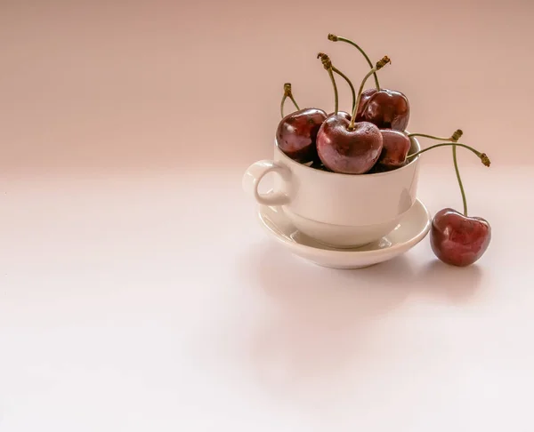 Closeup of a light cup filled with red sweet cherries on a light background.