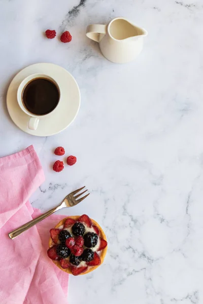 Dessert with fruits and cup of black coffee near to the jug of milk on a marble background. Top view. Copy space. Vertical orientation.