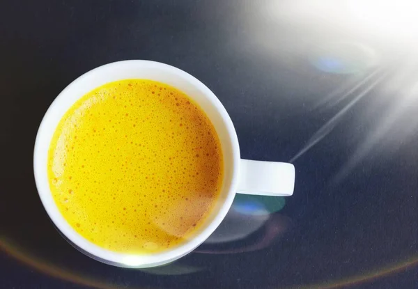 Golden (turmeric) milk in a white cup on the dark background. Top view.