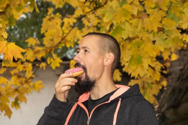 Happy man eating a donut and smiling on the autumn background.