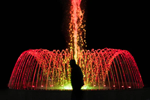 Renkli aydınlatma ile çeşme önünde yaşlı bir adamın silueti