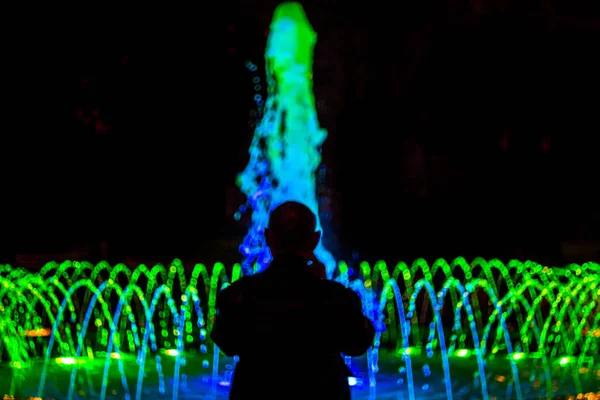 Renkli aydınlatma ile çeşme önünde yaşlı bir adamın silueti