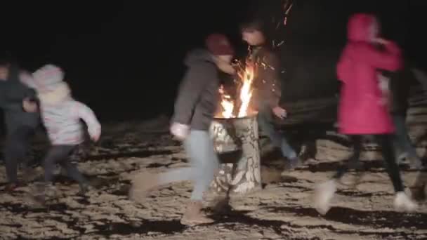 Дети бегают вокруг горящей бочки ночью — стоковое видео