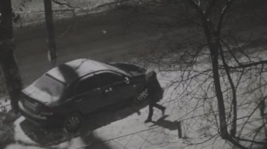 İnsanlar kışın park halindeki arabanın yanında yürürler. Karlı bir gecede sokak lambası direğinin altında.