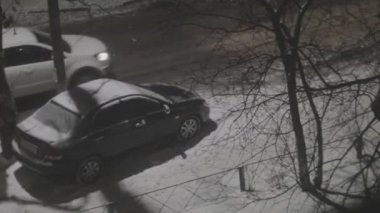 İnsanlar kışın park halindeki arabanın yanında yürürler. Karlı bir gecede sokak lambası direğinin altında.