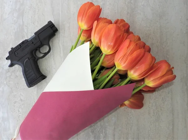 Um buquê de tulipas e uma pistola preta de 9 mm em um fundo cinza. O conceito do presente . — Fotografia de Stock