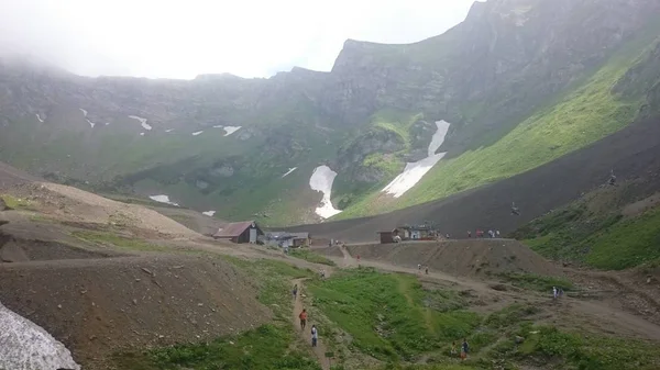 Panorama des montagnes et de la crête d'Aibga avec nuages bas. Restes de neige et d'herbe verte fraîche sur les montagnes près de la station de ski Rosa Khutor à Krasnaya Polyana. Sotchi, Russie . — Photo