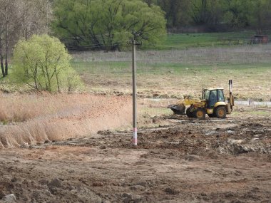 Nehre, ağaçlara ve gökyüzüne karşı şantiyede traktör