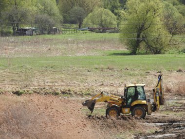 Nehre, ağaçlara ve gökyüzüne karşı şantiyede traktör
