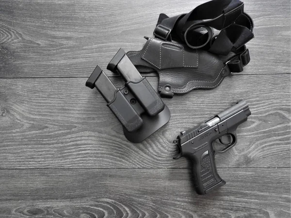 Pistola preta em coldre e revistas com fundo de madeira resistido — Fotografia de Stock