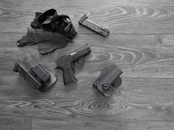 Gun black, spare magazines and leather holster on grey background.