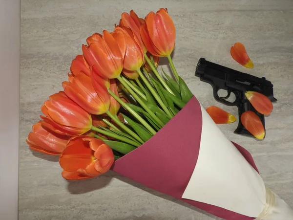 Zwarte pistool en een boeket, bloemblaadjes van tulpen, concept kaarten voor mannen — Stockfoto