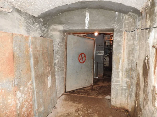 Una prisión abandonada en un búnker subterráneo. Un antiguo refugio soviético de bombas de guerra fría. La puerta cerrada del búnker. Tuberías y válvulas. Condiciones de poca luz. Búnker de miedo y pesadillas . Imagen de stock