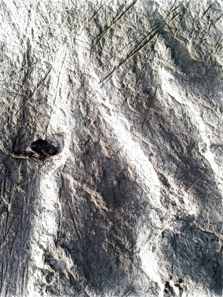 Uma pequena pedra negra na areia. A superfície irregular da praia é cortada por listras lisas e crateras de forma rasgada. Textura desenho artístico. Arte desenhar sombras suaves estilo . — Fotografia de Stock