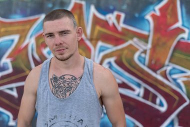 Duvarında grafiti olan spor tişörtlü bir kabadayı.