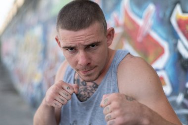 Duvarında grafiti olan spor tişörtlü bir kabadayı.