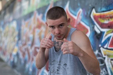 Duvarında grafiti olan spor tişörtlü bir kabadayı.