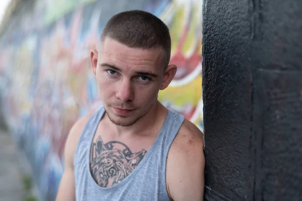 Un bravucón con camisa deportiva cerca de una pared con graffiti — Foto de Stock