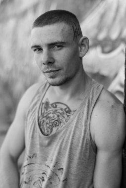 Duvarında grafiti olan spor tişörtlü bir kabadayı. Siyah beyaz fotoğraf. BW