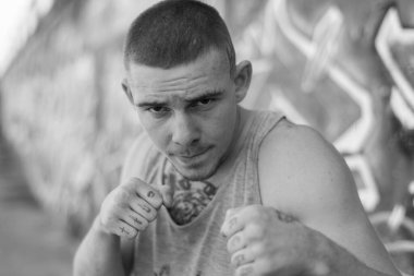 Duvarında grafiti olan spor tişörtlü bir kabadayı. Siyah beyaz fotoğraf. BW