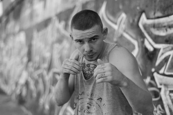 Un bravucón con camisa deportiva cerca de una pared con graffiti. Foto en blanco y negro. BW —  Fotos de Stock