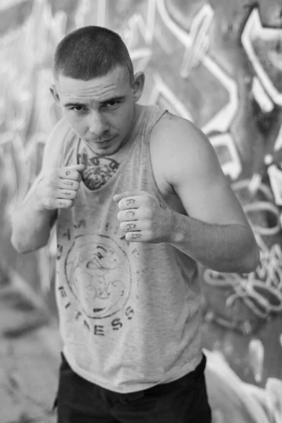 Un bravucón con camisa deportiva cerca de una pared con graffiti. Foto en blanco y negro. BW —  Fotos de Stock