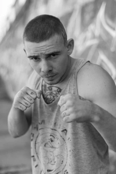 Un bravucón con camisa deportiva cerca de una pared con graffiti. Foto en blanco y negro. BW —  Fotos de Stock