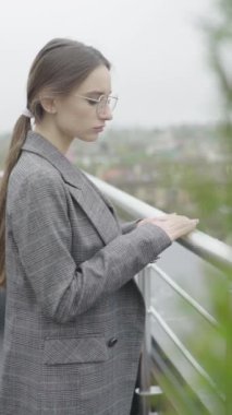 Dikey video. Gözlüklü ve gri takım elbiseli güzel bir kız. Yavaş çekim