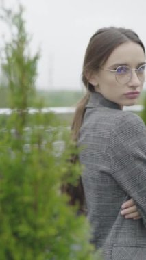 Dikey video. Gözlüklü ve gri takım elbiseli güzel bir kız. Yavaş çekim