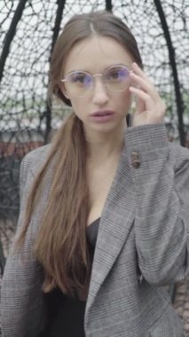 Dikey video. Gözlüklü ve gri takım elbiseli güzel bir kız. Yavaş çekim