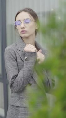 Dikey video. Gözlüklü ve gri takım elbiseli güzel bir kız. Yavaş çekim