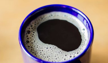 Turuncu ışıklı arka planda mavi bardakta hazır kahve. İyi sabahlar. Sabah sade kahve..