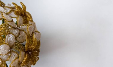 Gri arka planda boncuklardan beyaz çiçeklerle süslenmiş altın bir buket. Arka planda çiçekler.