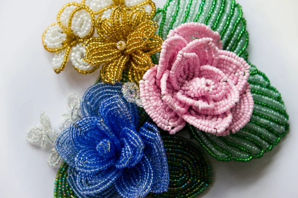 Beaded flowers on a white background. Blue bead flower, pink bead flower, yellow bead flower. Flowers from beads. Three flower from beads on a white background.