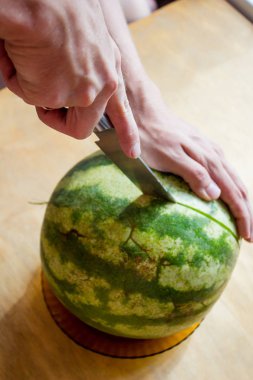 Bir adam karpuz keser. Erkeklerin elleri bir bıçakla masaya karpuz kesiyor. Boşluğu kopyala, üst görünüm, düz uzanma