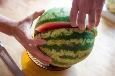 Bir adam karpuz keser. Erkeklerin elleri bir bıçakla masaya karpuz kesiyor. Bir adam karpuzu parçalara ayırır. Boşluğu kopyala, üst görünüm, düz uzanma