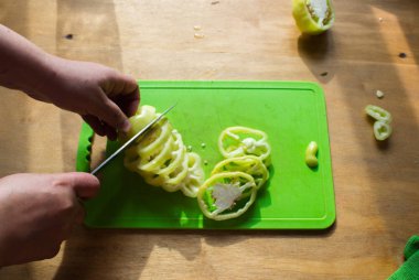 Kadın elleri yeşil biberi bıçakla kesiyor. Masada dilimlenmiş biber. Yeşil arka planda biber. Mutfak geçmişi. Düz konum, üst görünüm, kopyalama alanı