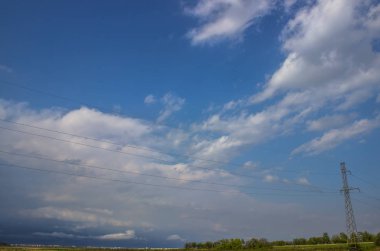 Gökyüzü masmavi, sirrus bulutları ve elektrik hatları uzakta..
