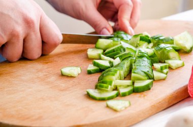 Kadın elleri tahta arka planda sebze kesiyor.