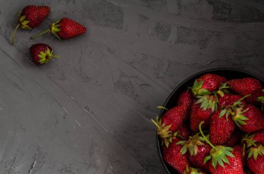 Gri bir concre üzerinde siyah bir tabakta taze yaz olgun çilek