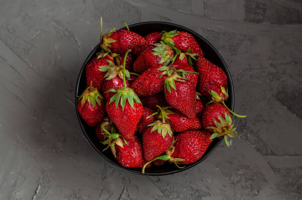Fresh summer ripe strawberries in a black plate on a gray concre