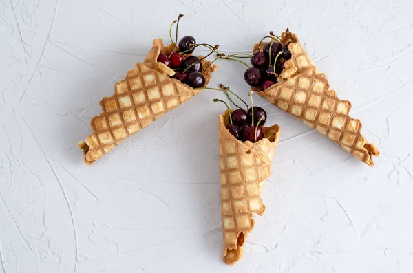 Ice cream cone filled with cherries on a light white concrete ba